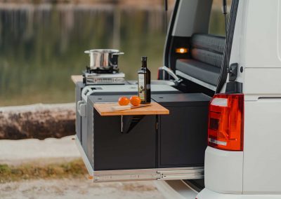 Campingküche auf dem Heckauszug mit Kühlbox und Becken und Kocher mit Hintergrund am See